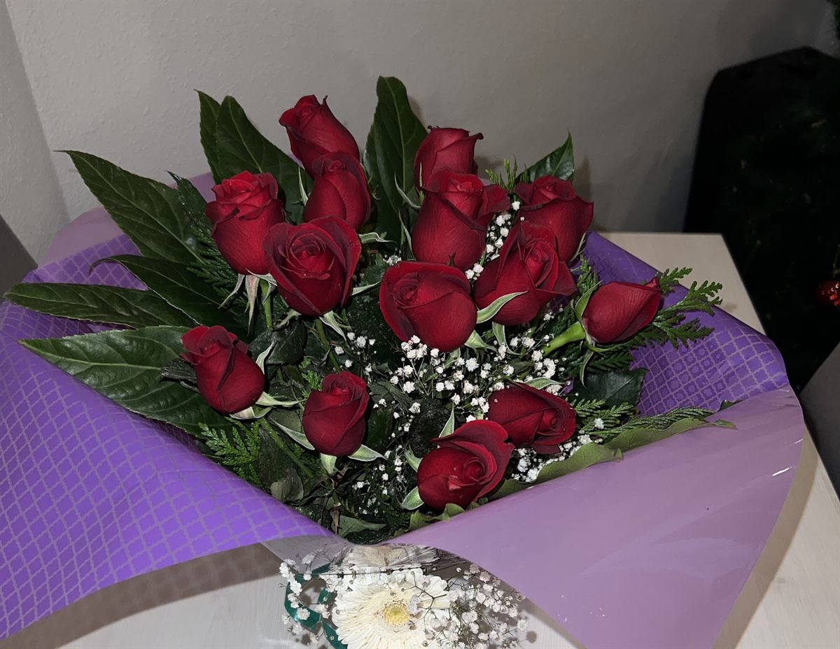 Docena de rosas rojas envuelta en papel lila